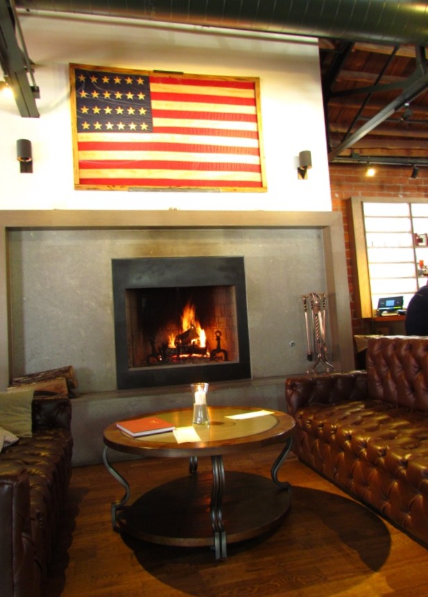 Two tufted leather sofas flank the fireplace. An antique American flag habgs above the fireplace as decoration.